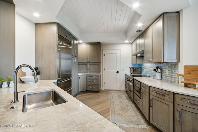 kitchen with built in fridge, tasteful backsplash, sink, light hardwood / wood-style floors, and a raised ceiling