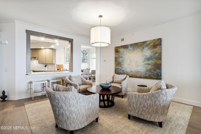 living room featuring wood-type flooring, ornamental molding, and sink