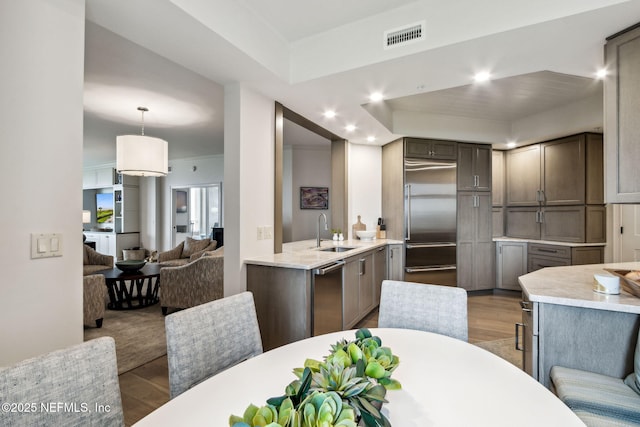 kitchen featuring appliances with stainless steel finishes, sink, hanging light fixtures, and light hardwood / wood-style flooring