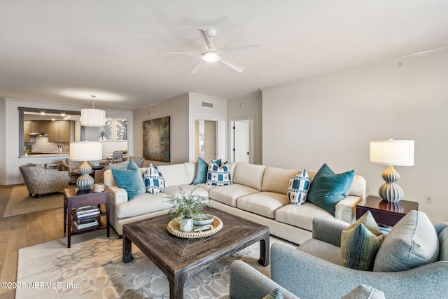 living room featuring ceiling fan, ornamental molding, and light wood-type flooring