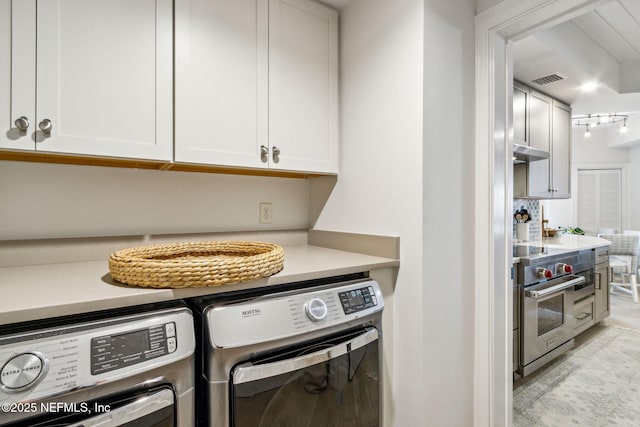 clothes washing area with cabinets and washing machine and clothes dryer