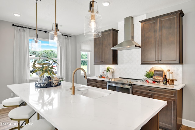 kitchen featuring stainless steel range with electric stovetop, wall chimney range hood, decorative light fixtures, and sink