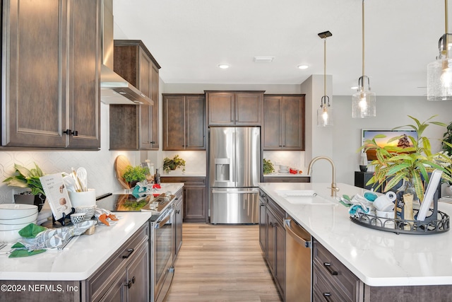 kitchen featuring sink, appliances with stainless steel finishes, dark brown cabinets, decorative light fixtures, and wall chimney exhaust hood