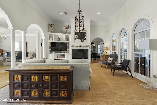 carpeted living room featuring ornamental molding, a tiled fireplace, decorative columns, and a wealth of natural light