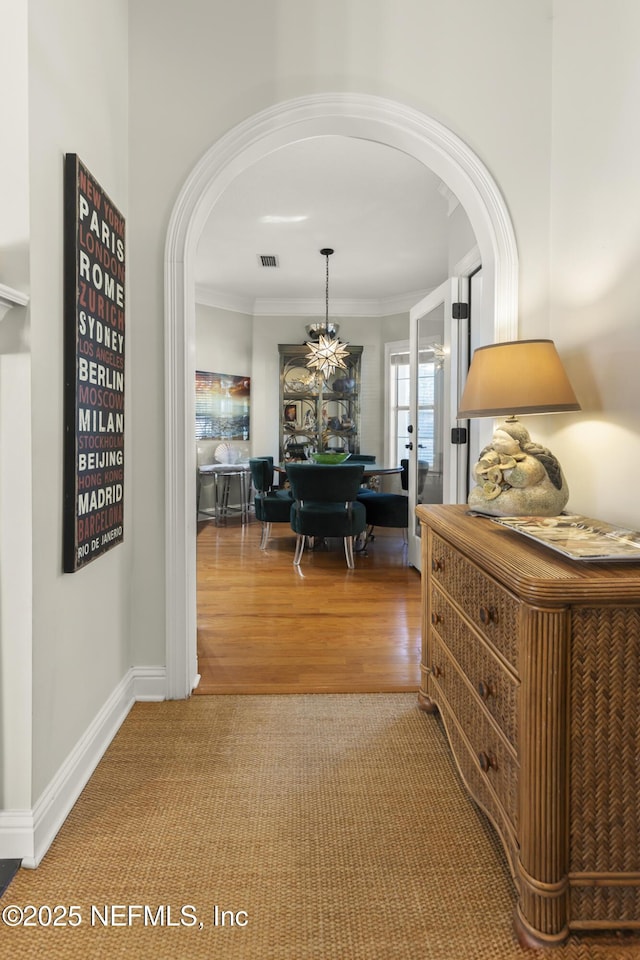 hall with arched walkways, wood finished floors, visible vents, baseboards, and crown molding