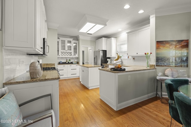 kitchen featuring light wood finished floors, appliances with stainless steel finishes, a peninsula, light stone countertops, and crown molding