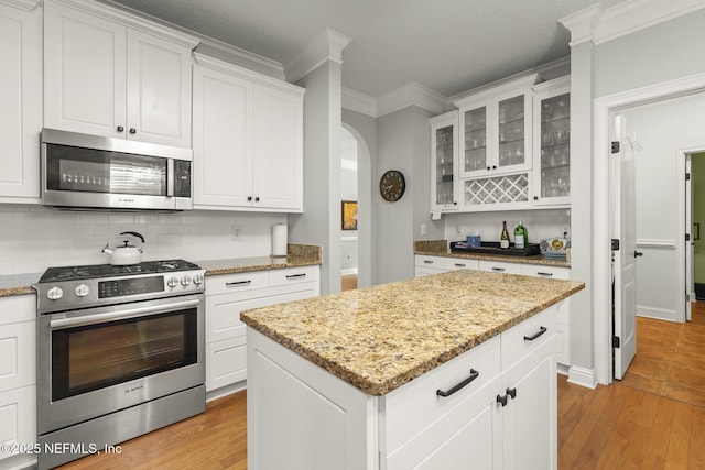 kitchen with light wood-type flooring, ornamental molding, stainless steel appliances, and backsplash