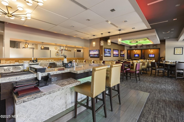 kitchen featuring light stone countertops, pendant lighting, a drop ceiling, and a kitchen breakfast bar