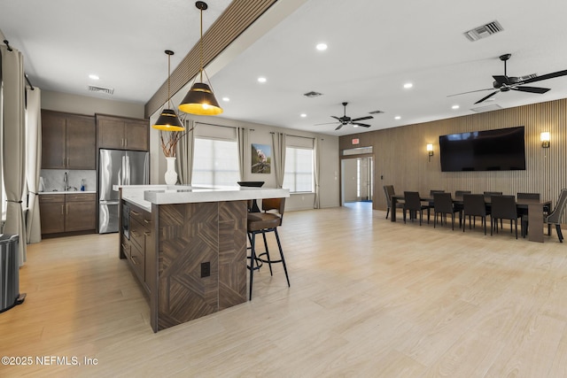 kitchen with decorative light fixtures, a center island, dark brown cabinets, light wood-type flooring, and stainless steel fridge