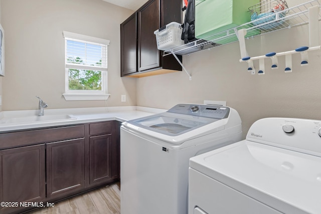 laundry room with cabinets, sink, washing machine and dryer, and light hardwood / wood-style flooring