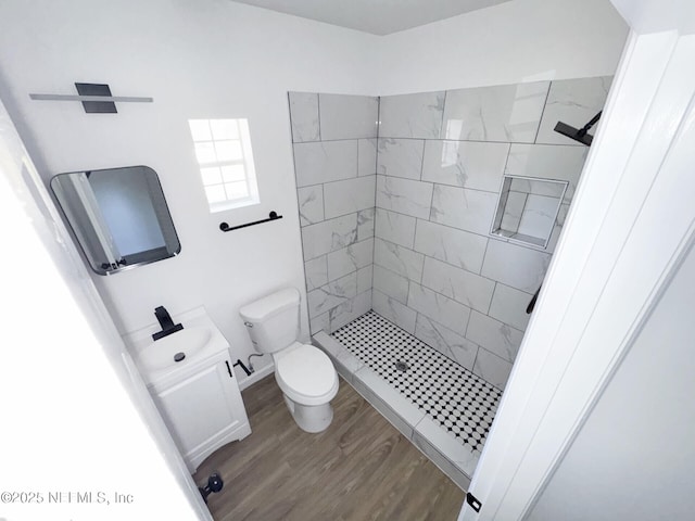 bathroom with wood-type flooring, toilet, vanity, and a tile shower