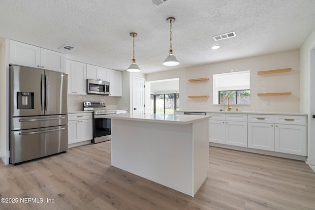 kitchen featuring stainless steel appliances, white cabinetry, hanging light fixtures, and sink