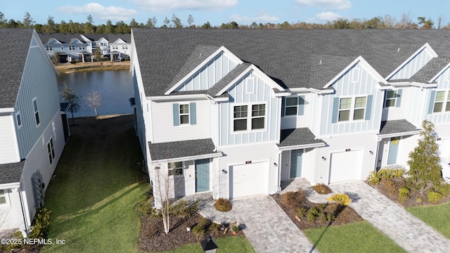 view of front of house featuring decorative driveway, roof with shingles, a water view, board and batten siding, and a residential view