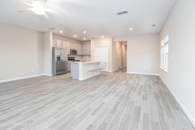 kitchen with a center island with sink, visible vents, open floor plan, stainless steel appliances, and light countertops