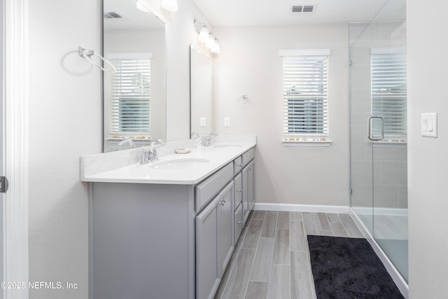 full bathroom with wood finish floors, a sink, visible vents, double vanity, and a stall shower