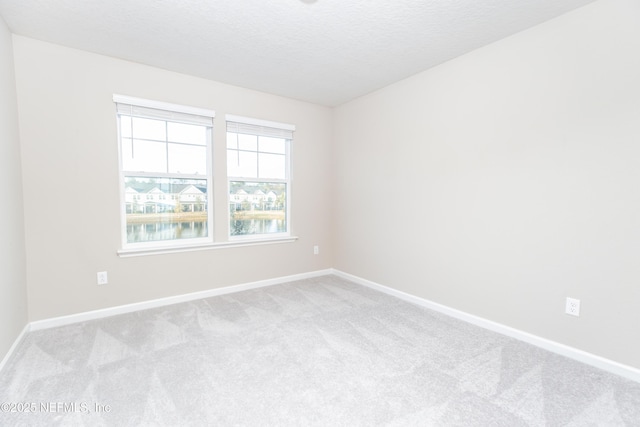 spare room featuring baseboards, a textured ceiling, and light colored carpet