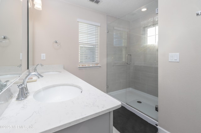 bathroom featuring double vanity, a stall shower, visible vents, and a sink