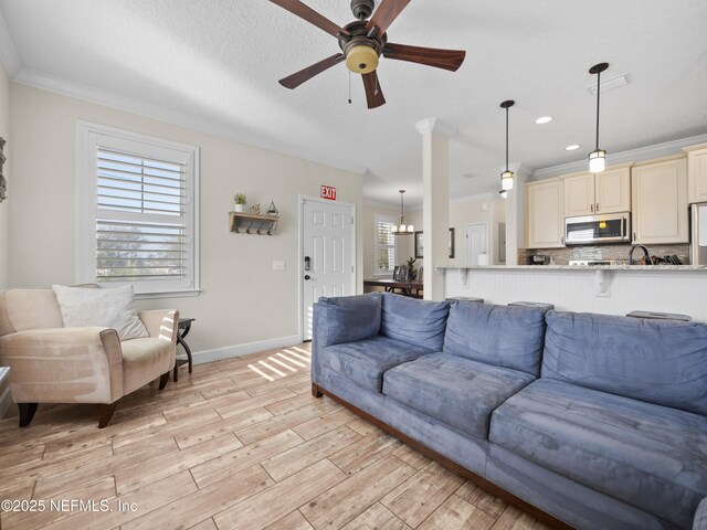 living room with crown molding, ceiling fan with notable chandelier, a wealth of natural light, and light hardwood / wood-style flooring