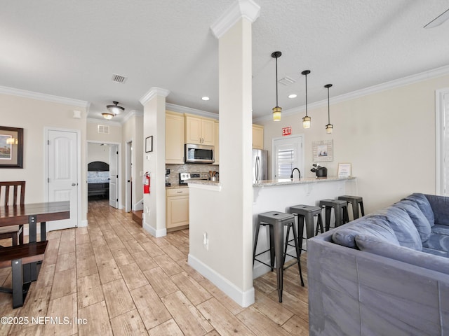 kitchen featuring cream cabinets, crown molding, kitchen peninsula, and appliances with stainless steel finishes