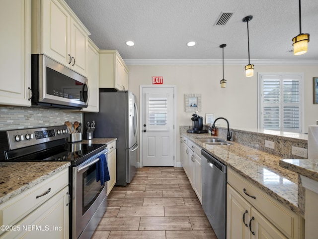 kitchen with pendant lighting, sink, ornamental molding, stainless steel appliances, and cream cabinetry