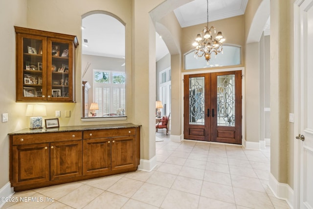 entrance foyer with an inviting chandelier, ornamental molding, french doors, and light tile patterned flooring