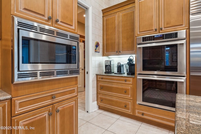 kitchen with tasteful backsplash, tile walls, light tile patterned floors, appliances with stainless steel finishes, and light stone countertops