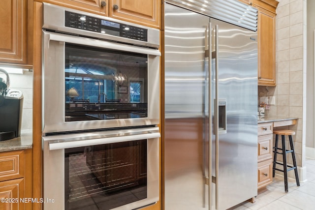 kitchen with light stone counters, backsplash, light tile patterned floors, and appliances with stainless steel finishes