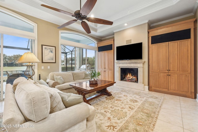 tiled living room with crown molding, a healthy amount of sunlight, a tray ceiling, and a premium fireplace