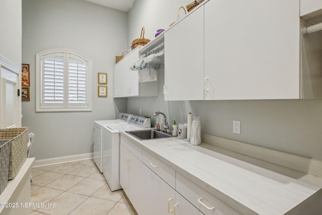 clothes washing area with light tile patterned floors, sink, washing machine and dryer, and cabinets