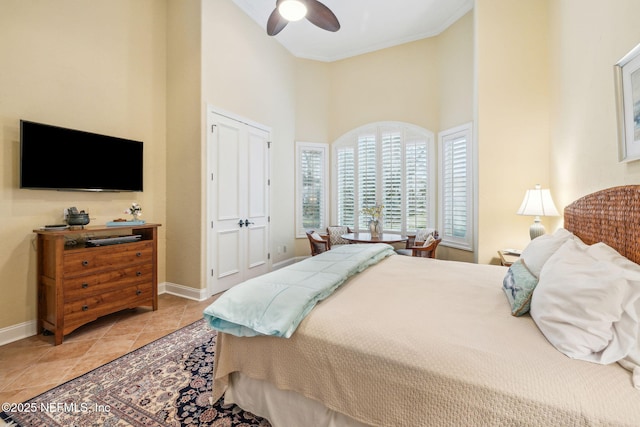 tiled bedroom with a high ceiling, crown molding, ceiling fan, and a closet