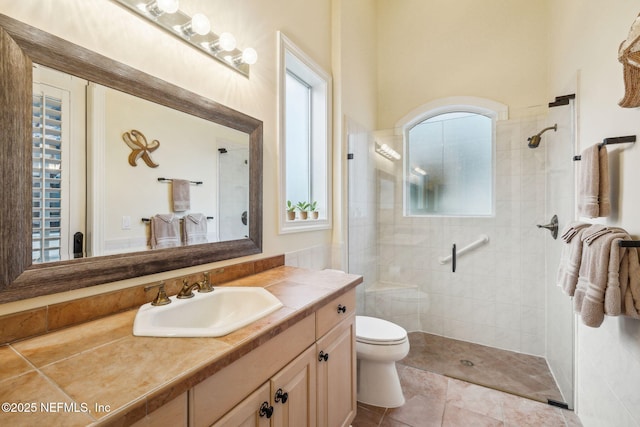 bathroom with tiled shower, a healthy amount of sunlight, vanity, and toilet