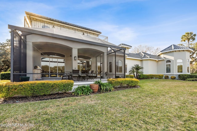 rear view of house with a patio, a balcony, glass enclosure, and a lawn