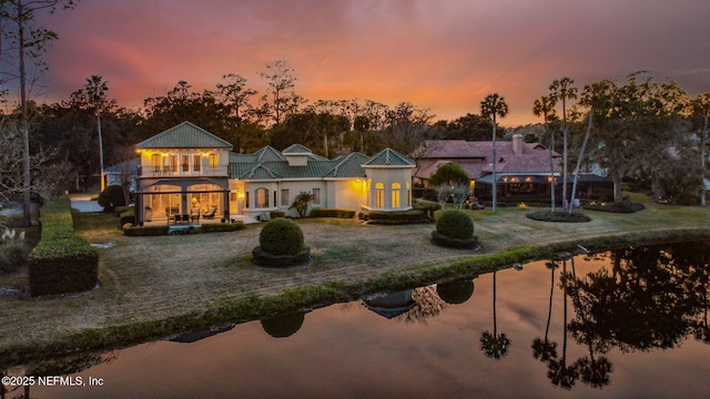 back house at dusk with a balcony and a lawn