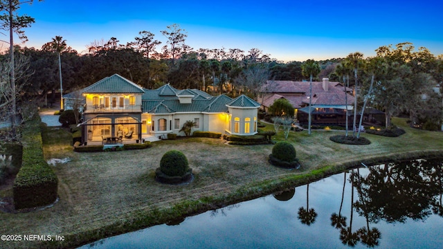 back house at dusk featuring a yard, a balcony, and a water view