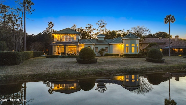 back house at dusk with a water view and a balcony