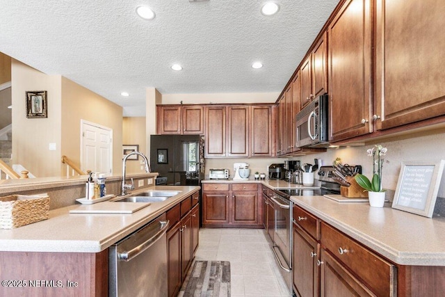 kitchen featuring sink, a kitchen island with sink, light tile patterned floors, stainless steel appliances, and a textured ceiling