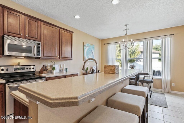 kitchen featuring light tile patterned flooring, stainless steel appliances, a kitchen bar, and a textured ceiling