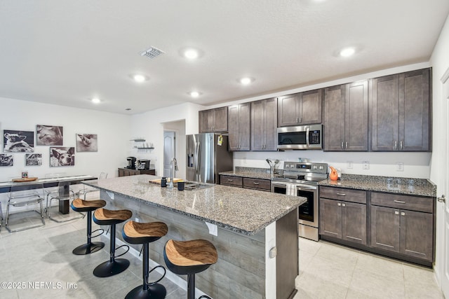 kitchen with an island with sink, sink, a kitchen bar, dark stone counters, and stainless steel appliances