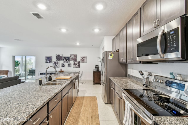 kitchen with sink, appliances with stainless steel finishes, dark brown cabinets, light stone countertops, and light tile patterned flooring