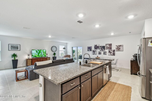 kitchen with dark brown cabinetry, sink, light stone counters, a center island with sink, and stainless steel appliances