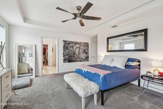 carpeted bedroom featuring ceiling fan, ensuite bathroom, a raised ceiling, a walk in closet, and a closet