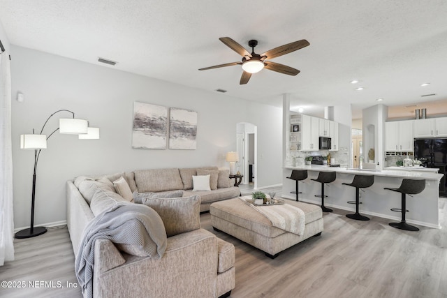 living room with ceiling fan, a textured ceiling, and light wood-type flooring