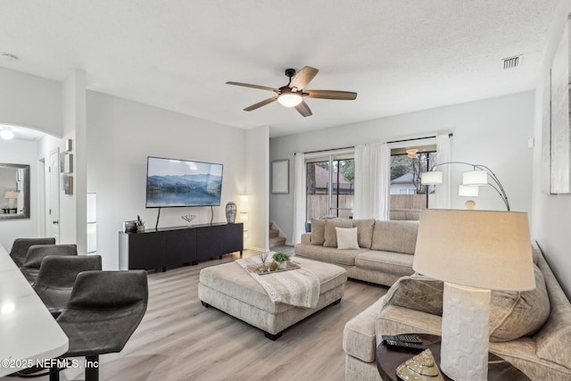 living room featuring ceiling fan, light hardwood / wood-style flooring, and a textured ceiling