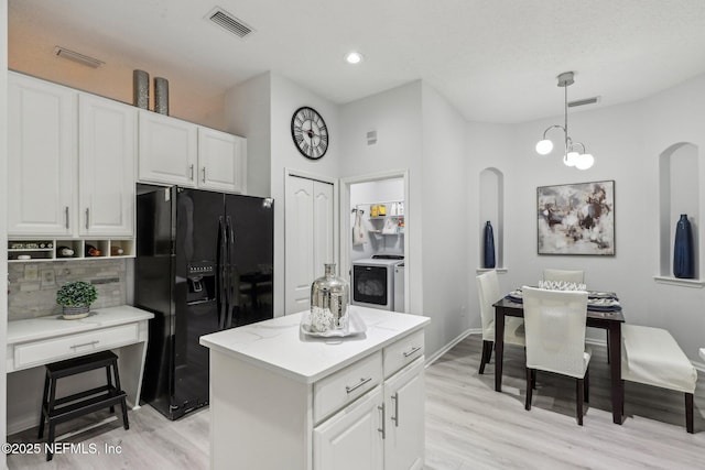 kitchen featuring hanging light fixtures, black fridge with ice dispenser, washer / dryer, and white cabinets