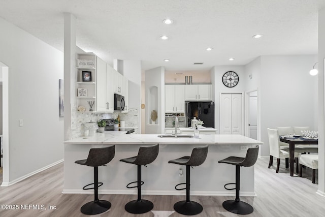 kitchen featuring black appliances, white cabinets, decorative backsplash, kitchen peninsula, and light wood-type flooring