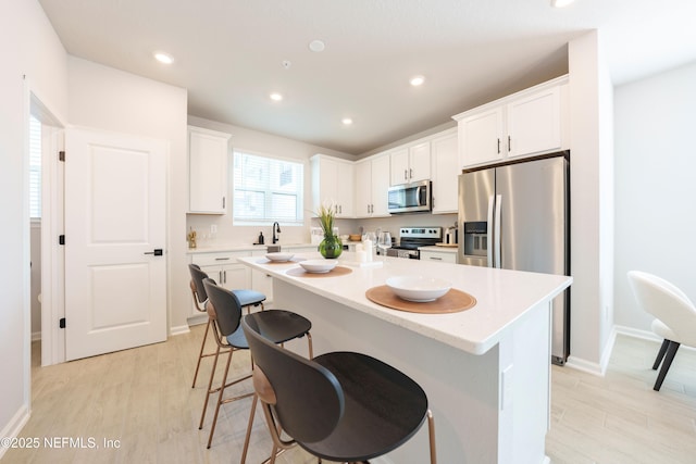 kitchen featuring a kitchen island, stainless steel appliances, light hardwood / wood-style floors, white cabinets, and a kitchen bar