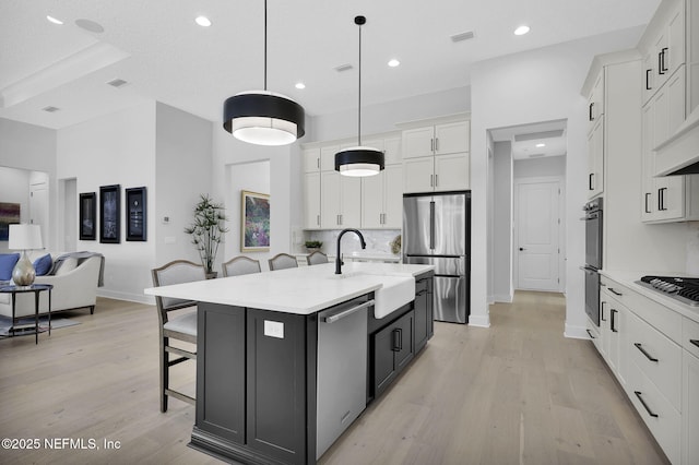 kitchen with a center island with sink, appliances with stainless steel finishes, a kitchen breakfast bar, decorative light fixtures, and white cabinets