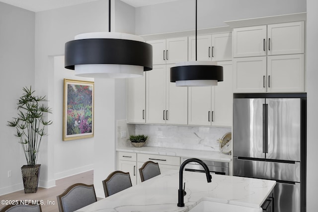 kitchen with tasteful backsplash, light stone counters, stainless steel refrigerator, and white cabinets