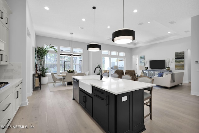 kitchen with light hardwood / wood-style flooring, hanging light fixtures, an island with sink, white cabinets, and sink