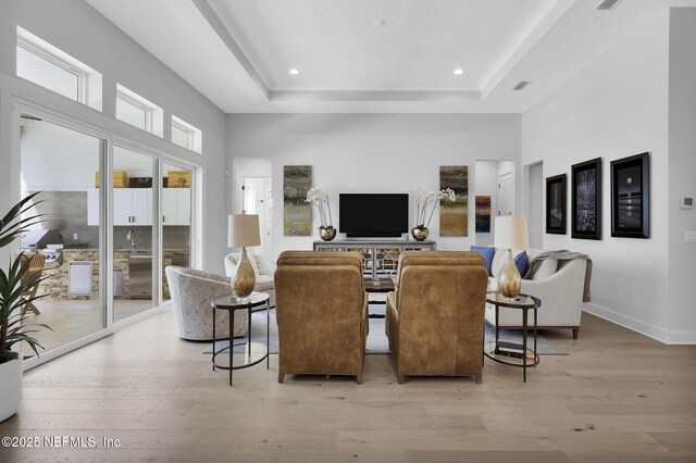 living room featuring a tray ceiling, sink, and light hardwood / wood-style floors